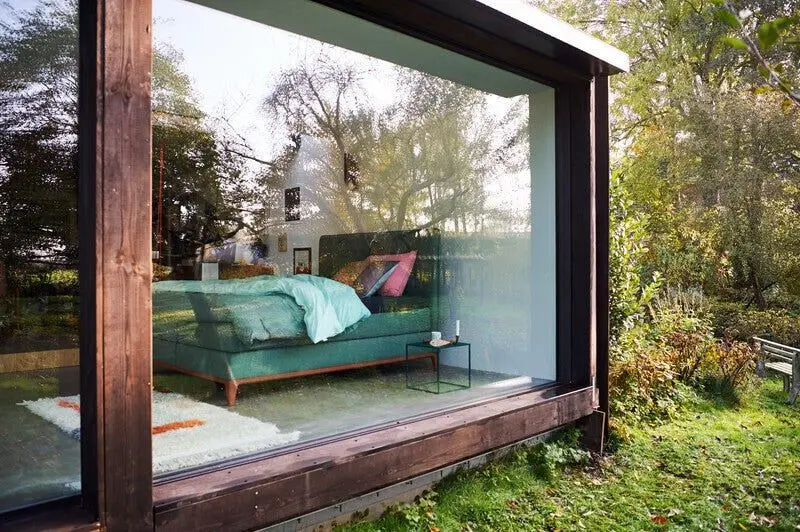 Groen Auping-bed achter een grote glaswand in een houten kader, met de tuin eromheen