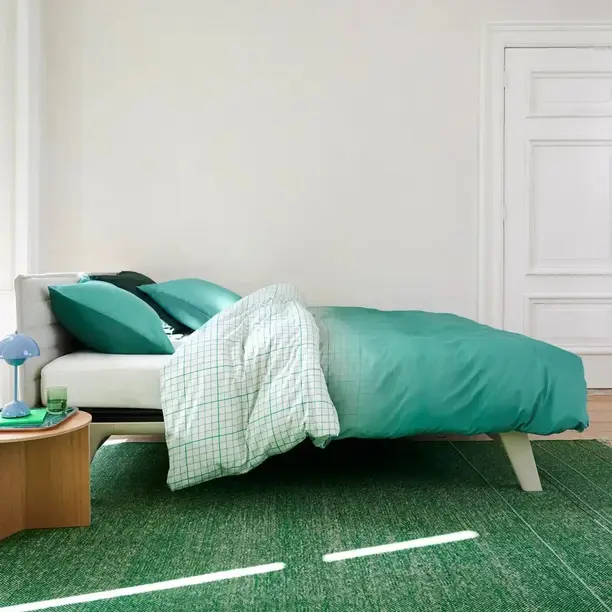 Groenblauw Auping-dekbedovertrek met een geruit laken op een licht bed en een groen vloerkleed