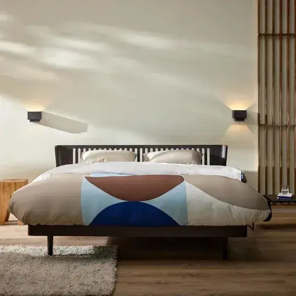 Auping-dekbedovertrek met grote ronde vlakken in zand, bruin en blauw op een donker houten bed