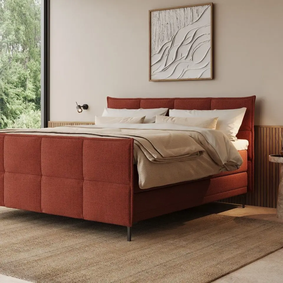 Terracotta gestoffeerde boxspring met hoofd- en voetbord in een lichte slaapkamer met een glaswand naar de tuin
