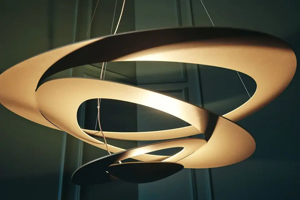Een gouden hanglamp in de vorm van een spiraal die naar beneden draait, voor een donkergroene wand