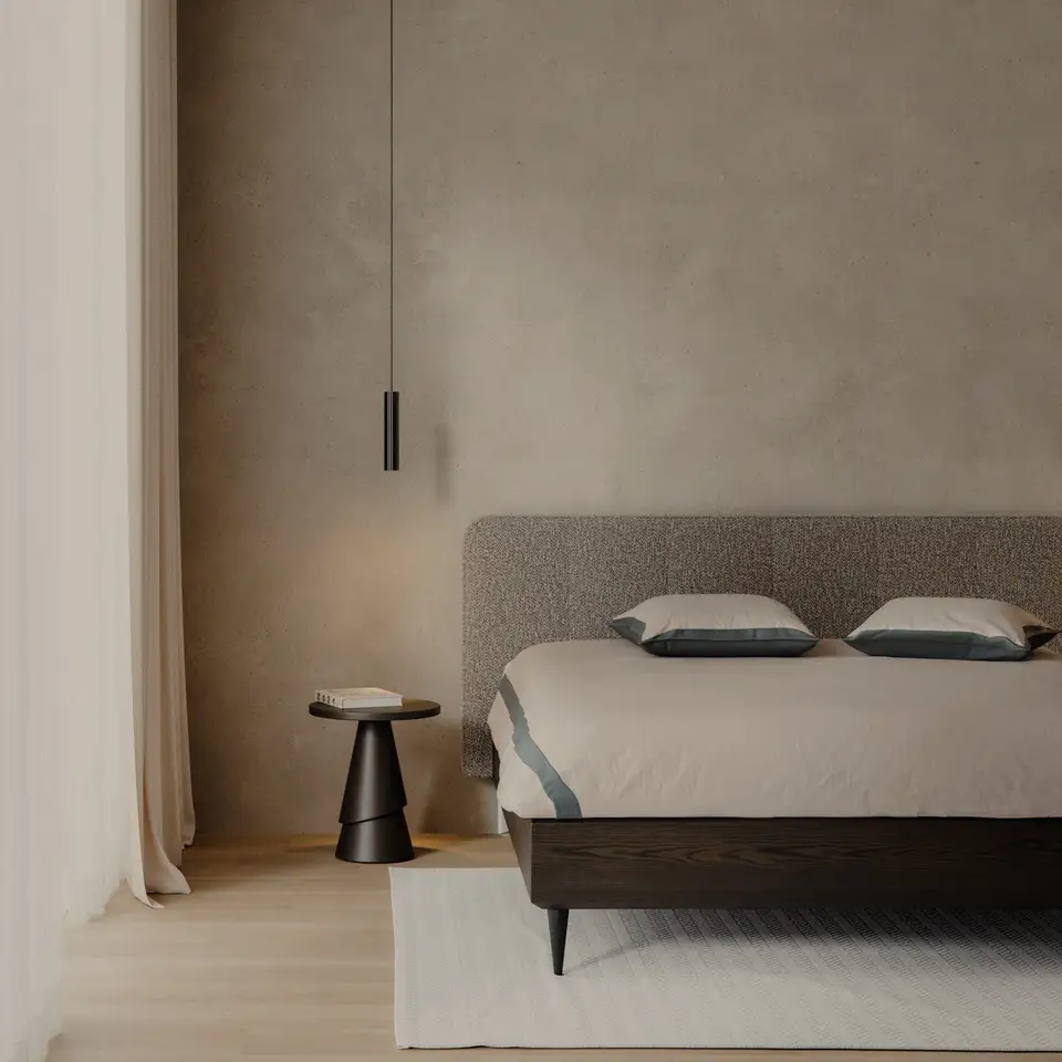 Gestoffeerd bed met een donker eiken frame tegen een warme kalkwand, met een zwarte hanglamp en een ronde bijzettafel
