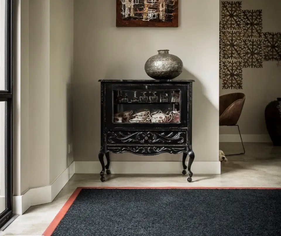 Donker wollen karpet met een terracotta rand voor een zwart antiek kastje