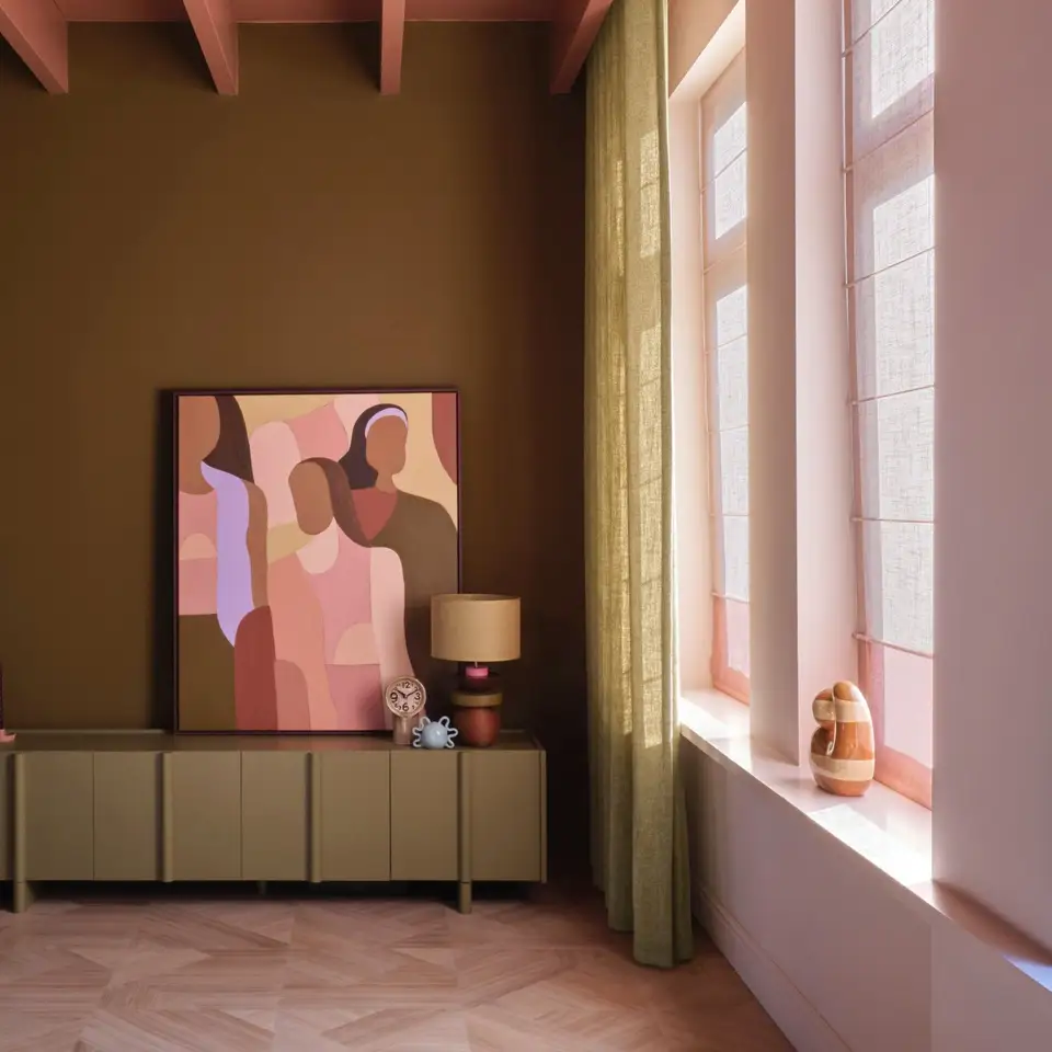 Kamer met een olijfgroene wand, een laag dressoir met een schilderij en een lamp, een linnen gordijn en roze vouwgordijnen voor hoge ramen, op een lichte houten vloer