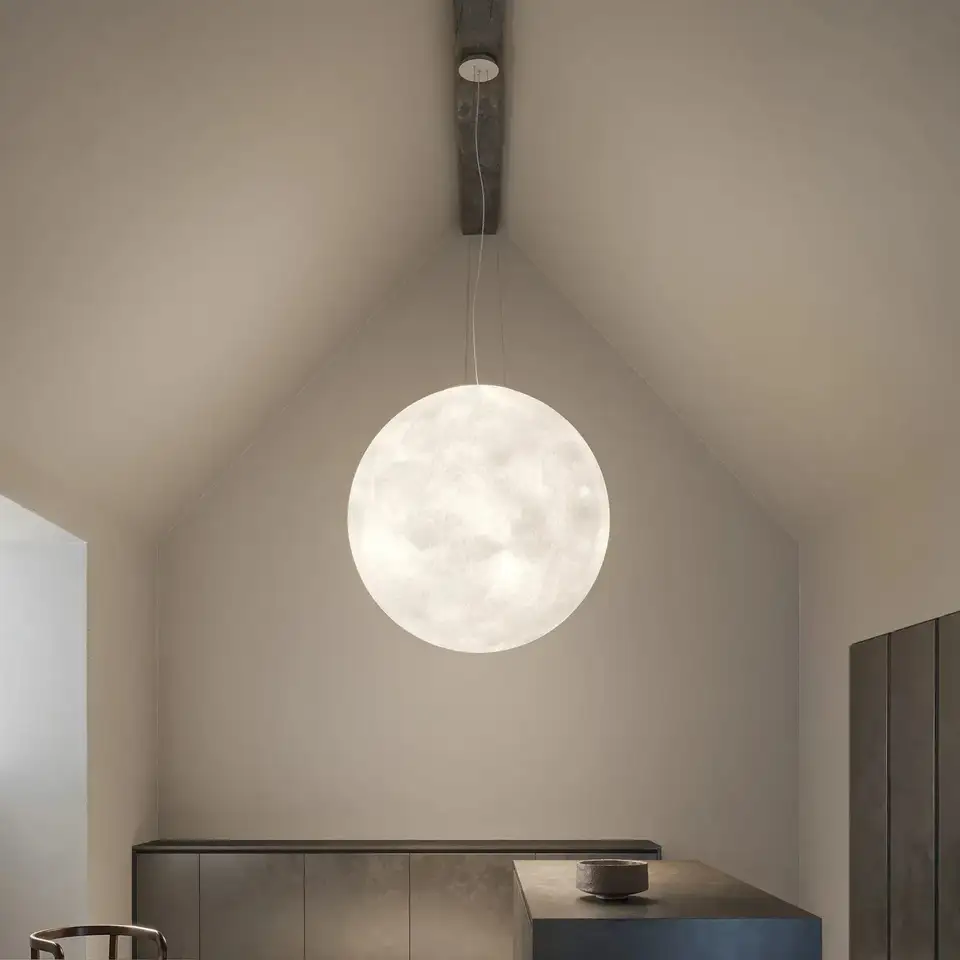 Een grote witte bollamp als een maan in een lichte kamer met een zadeldak, boven een donker keukenblok