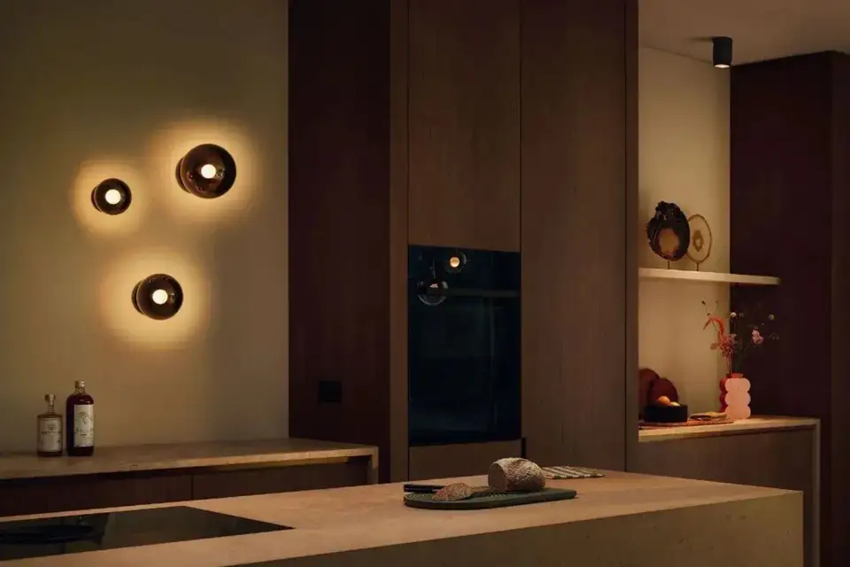 Drie wandlampen met een zachte lichtkrans op een warme wand in een donkere notenhouten keuken