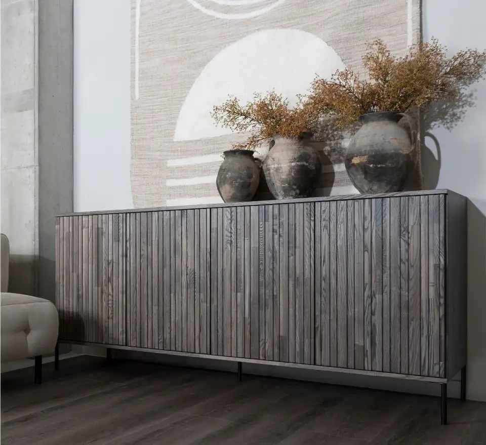 Houten dressoir met kruiken en droogbloemen op een donkere pvc-plankenvloer, voor een groot geweven wandkleed