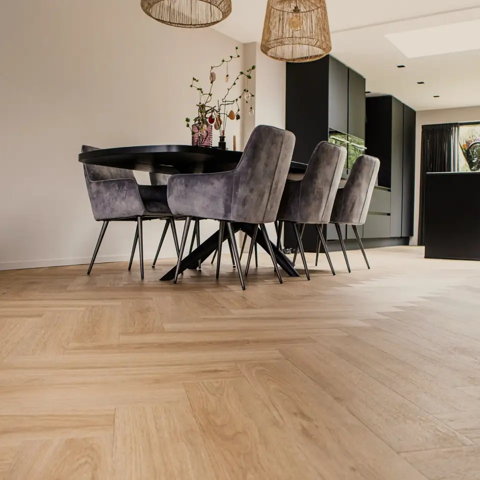 Lichte eiken visgraatvloer onder een eettafel met fluwelen stoelen