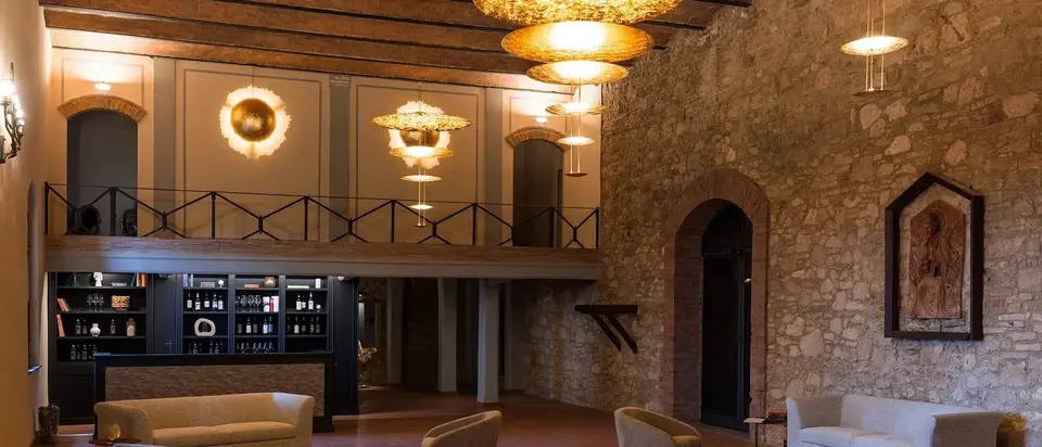 Hotellobby met gouden hanglampen en wandlampen tegen een muur van natuursteen, met lage fauteuils