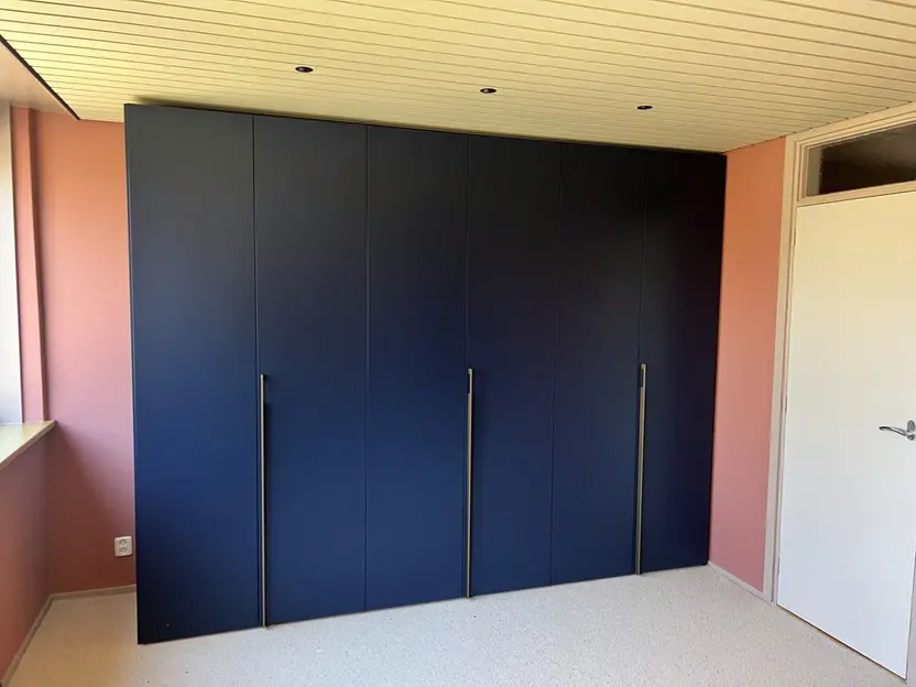 Donkerblauwe kledingkast over de hele wand van een slaapkamer, met de deuren dicht