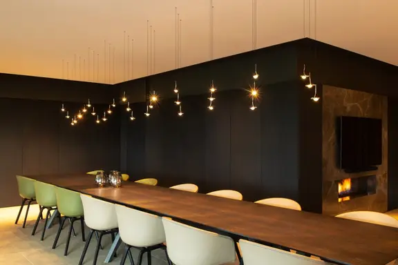 Een lange houten tafel in een donkere zaal onder tientallen kleine hanglampen die als sterren boven de tafel hangen