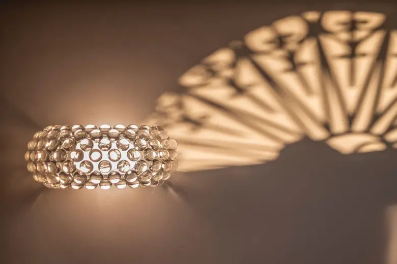 Een wandlamp van glazen bolletjes werpt een waaier van licht en schaduw op een warme wand