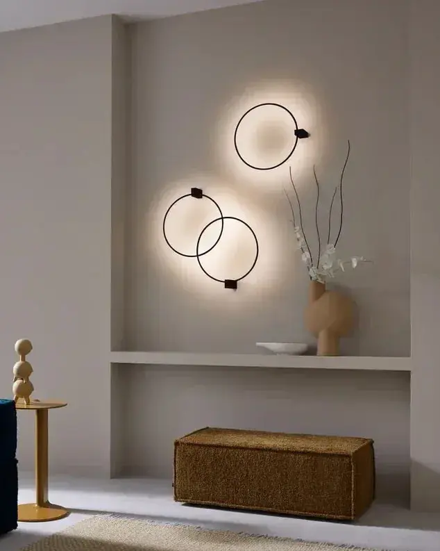 Twee ringvormige wandlampen met een zachte gloed boven een nis in een taupe woonkamer met een blauwe bank