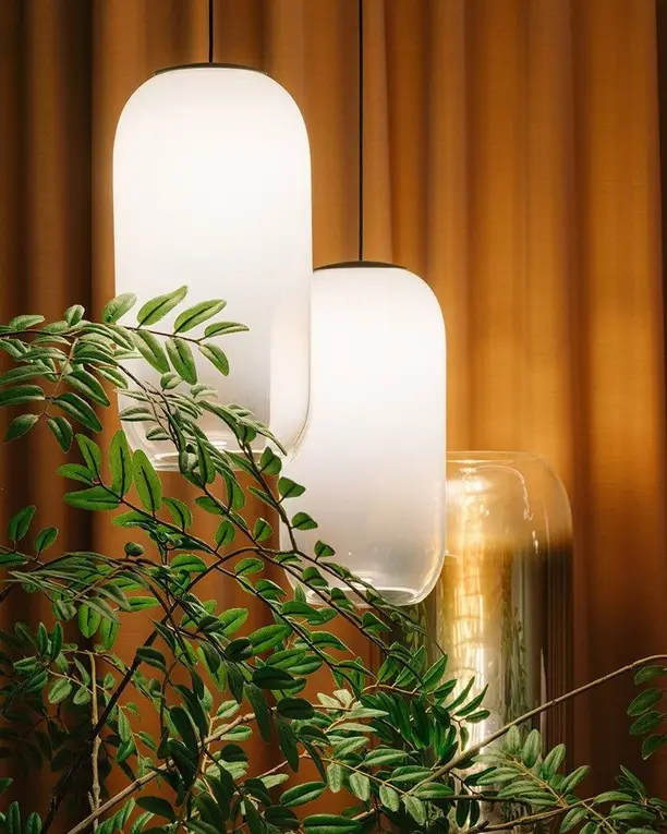 Twee hanglampen van opaalglas voor een amberkleurig gordijn, met groen blad ervoor