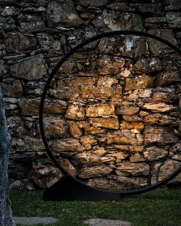 Een lichtring staat in het gras en verlicht een oude stenen muur