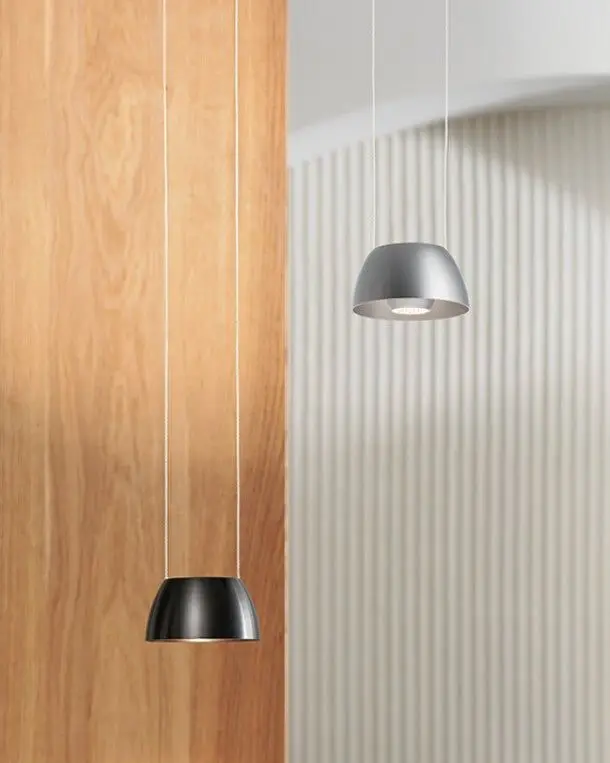 Twee hanglampen, een zwarte en een zilveren, voor een houten wand