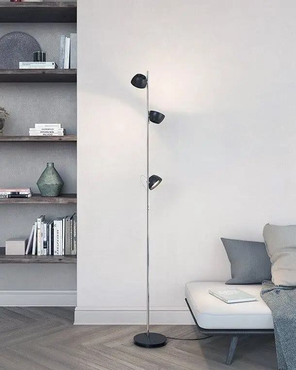 Een vloerlamp met drie zwarte koppen aan een stang naast een bank in een lichte kamer