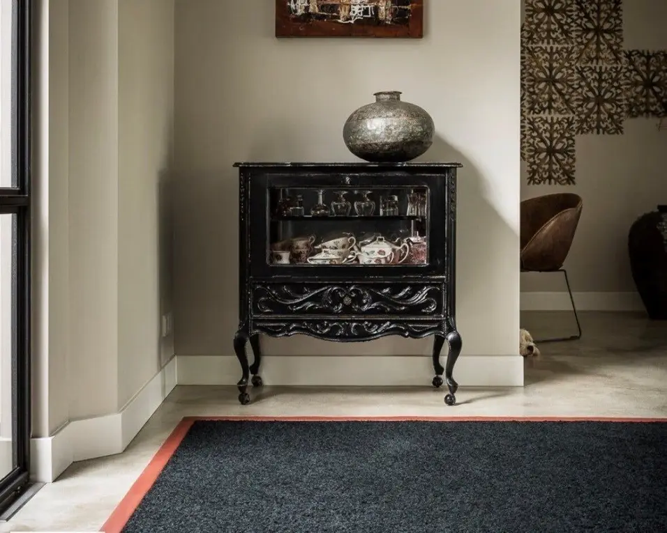 Donker wollen karpet met een terracotta rand voor een zwart antiek kastje