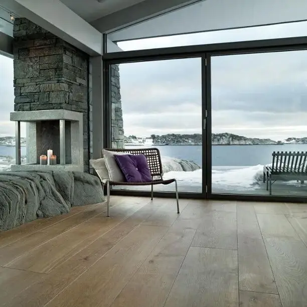Kamer met een stenen haard en grote ramen op zee, op brede eiken planken
