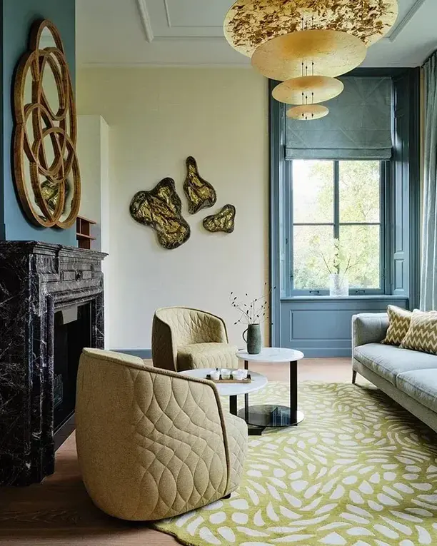 Een klassieke salon met marmeren schouw, gouden wandobjecten en een gelaagde gouden plafondlamp