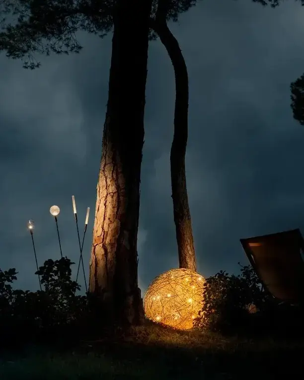 Een gloeiende bol van draad onder hoge bomen in een tuin bij avond