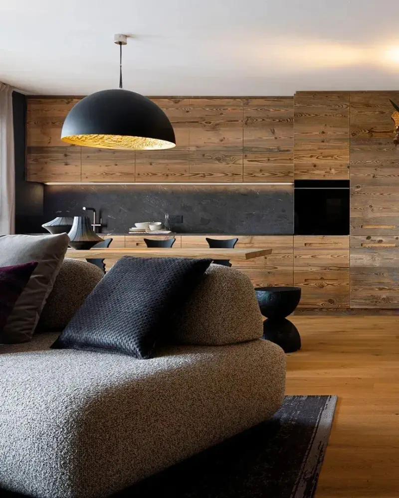 Een zwarte koepellamp met gouden binnenkant boven een zitkamer met houten wanden