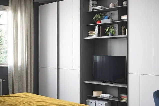 Witte kledingkast naast een open vakkenkast met een tv in een slaapkamer