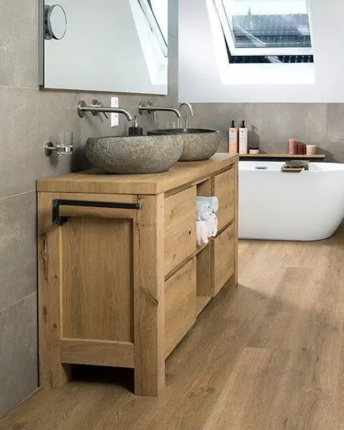 Badkamer met een eiken wastafelmeubel, stenen waskommen en een vrijstaand bad