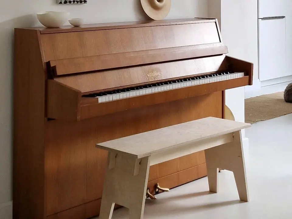Houten piano en een berkenhouten bankje op een witte vloer, met een kat en een fauteuil