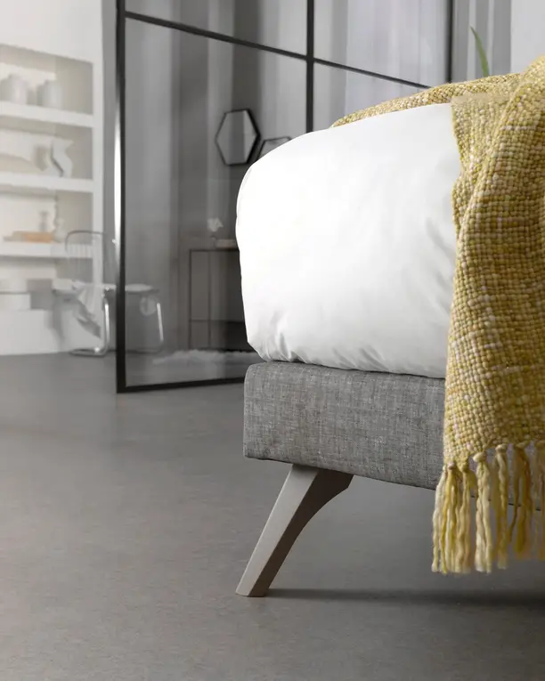 De box van een Balance-boxspring op een schuine houten poot, met een gele plaid