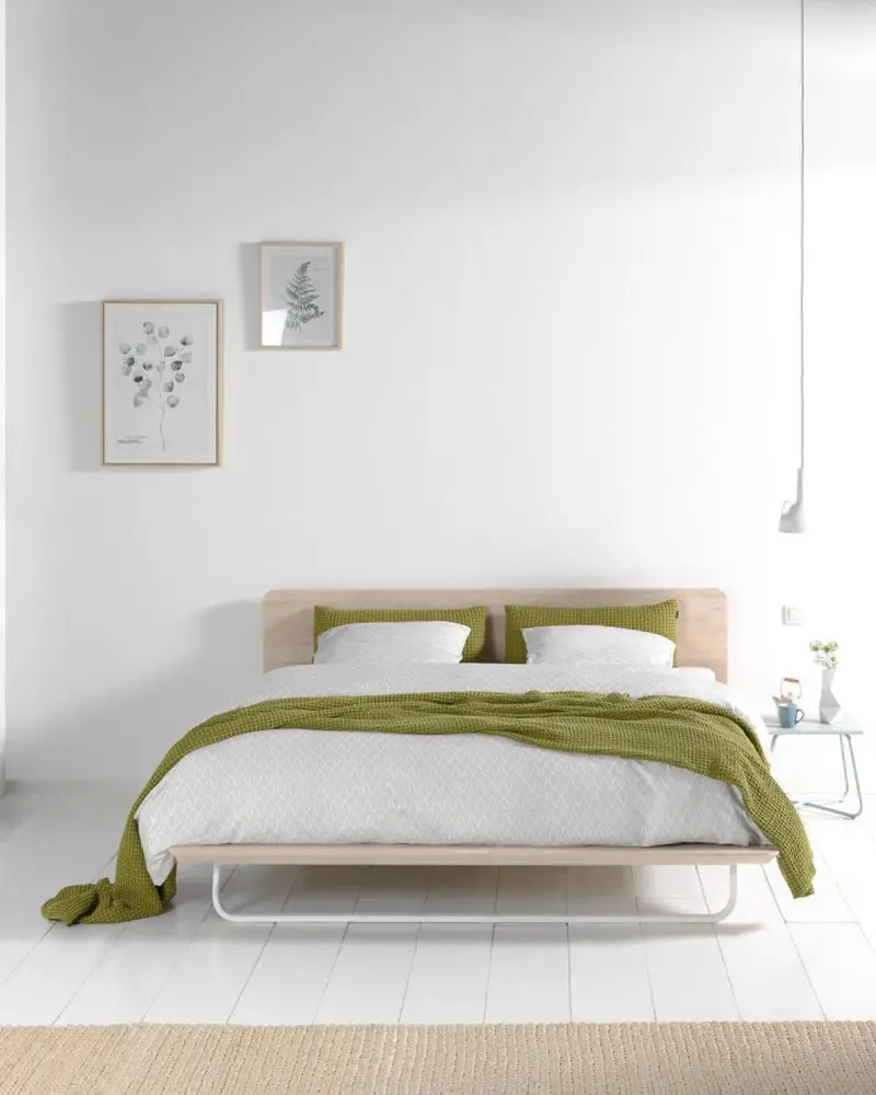 Het Less bed in naturel hout met een olijfgroene plaid in een witte kamer met planten