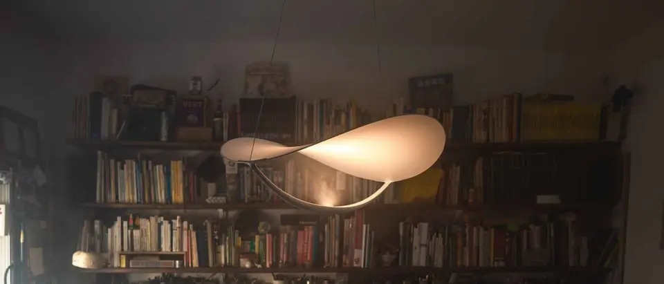 Een zwevende witte hanglamp in de vorm van een golvend blad voor een volle boekenwand