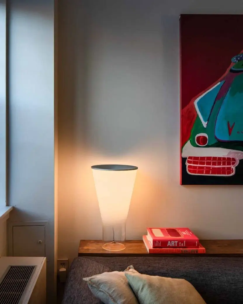 Een kegelvormige tafellamp op een lage kast naast een bank en een groot schilderij