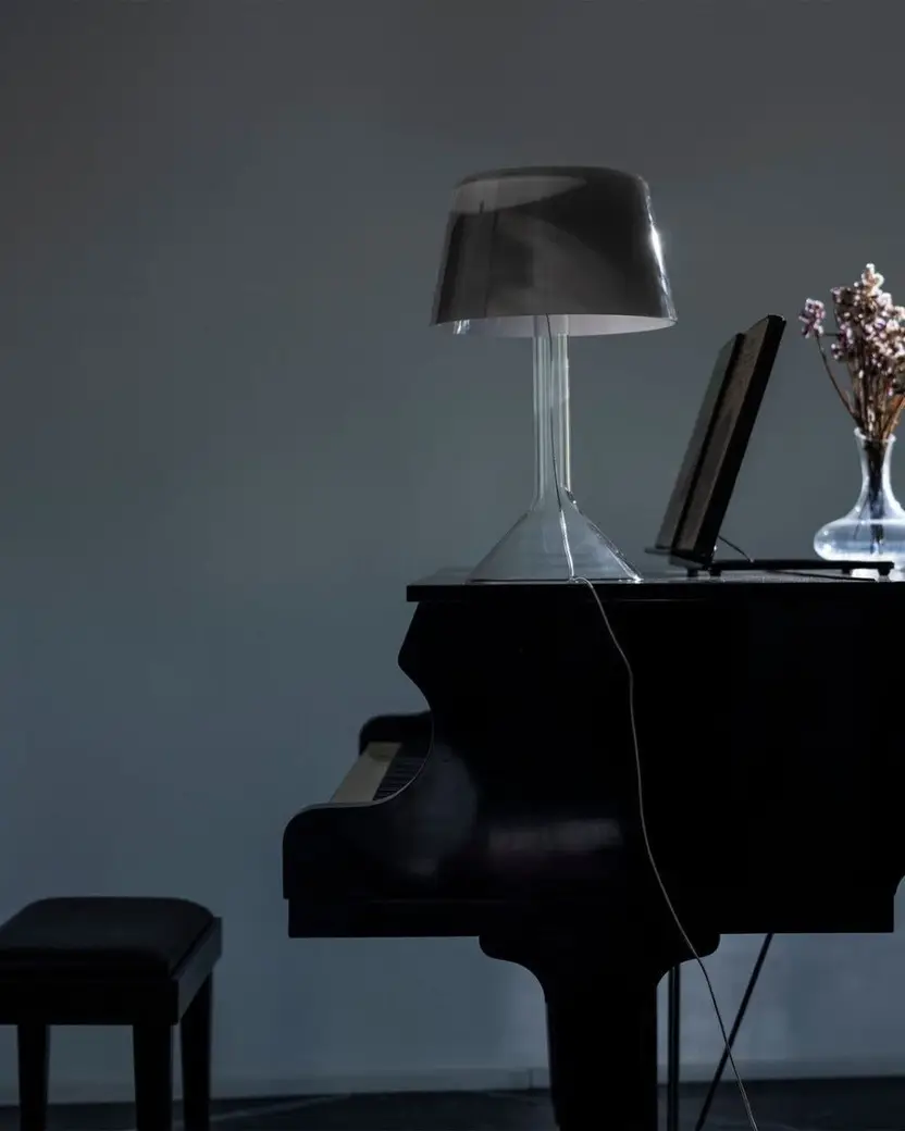 Een tafellamp met een glazen voet op een zwarte vleugel in een rustige kamer