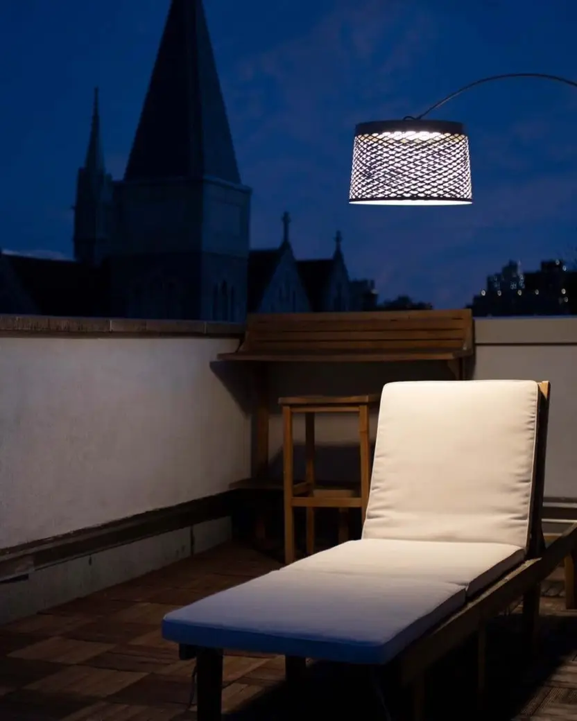 Een booglamp met een gevlochten kap boven een ligstoel op een dakterras bij avond