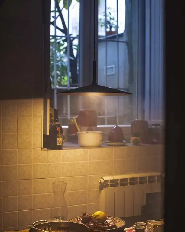 Een donkere betonnen hanglamp boven een aanrecht met tegels, in warm avondlicht