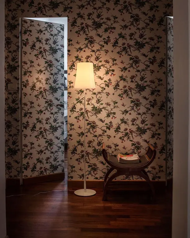 Een witte vloerlamp in een hoek met bloemetjesbehang en een donkere houten vloer