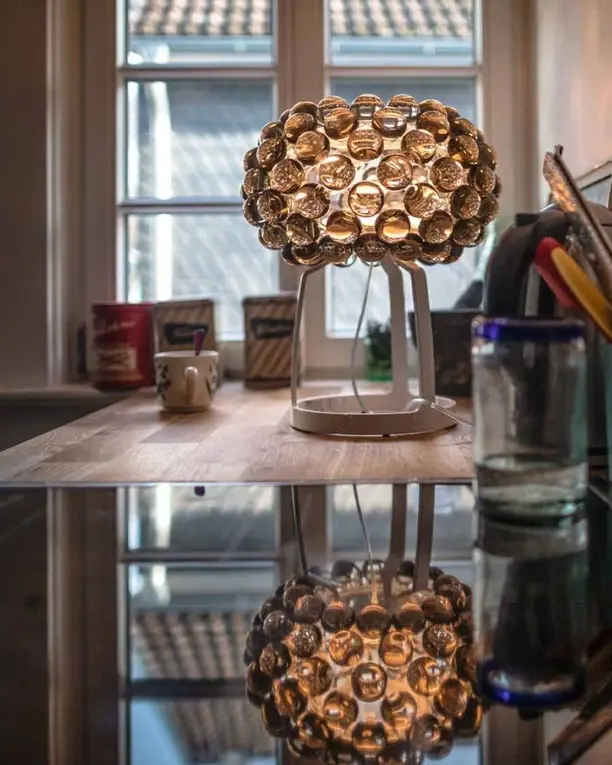 Een tafellamp van heldere bolletjes spiegelt in een glanzend keukenblad