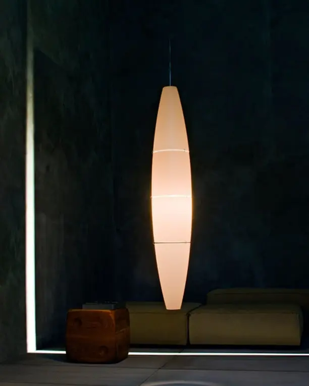 Een hoge, slanke witte lichtzuil in een donkere kamer met een lage bank