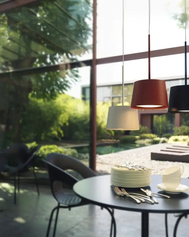 Drie hanglampen in rood, zwart en wit boven een ronde tafel in een tuinkamer