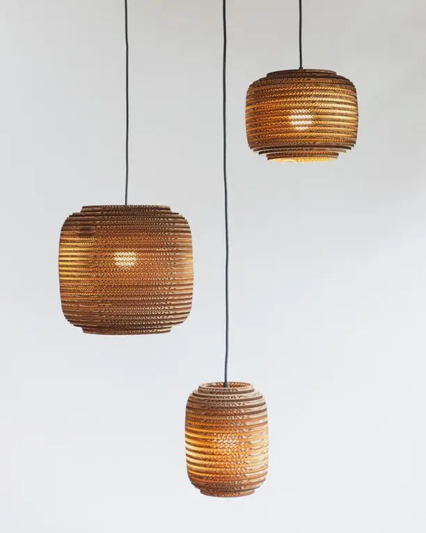 Drie kartonnen hanglampen op verschillende hoogtes voor een witte wand