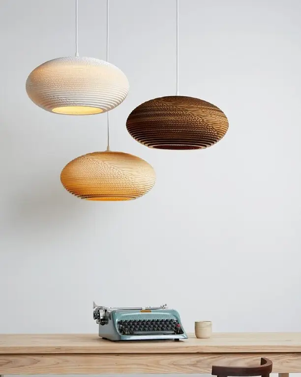 Drie platte hanglampen van karton boven een houten bureau met een typemachine