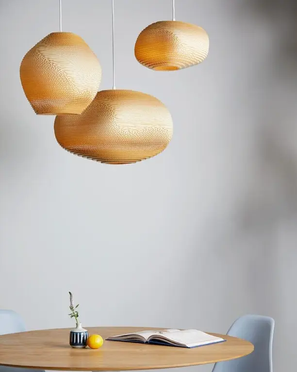 Drie lampen van karton in de vorm van kiezels boven een ronde tafel