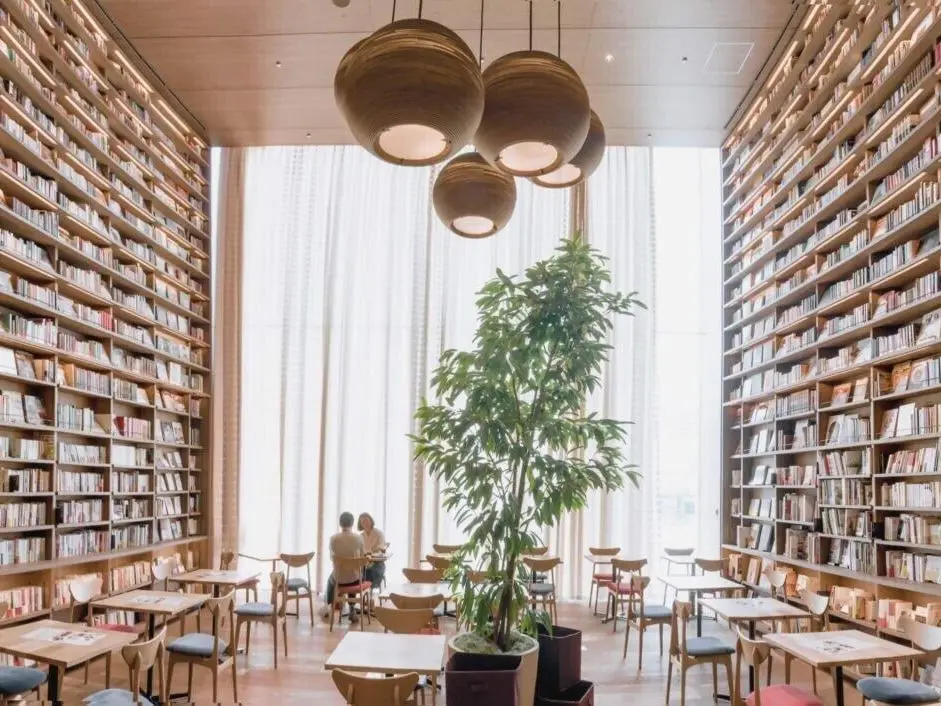 Bolvormige hanglampen van karton boven leestafels in een hoge bibliotheek met boekenwanden