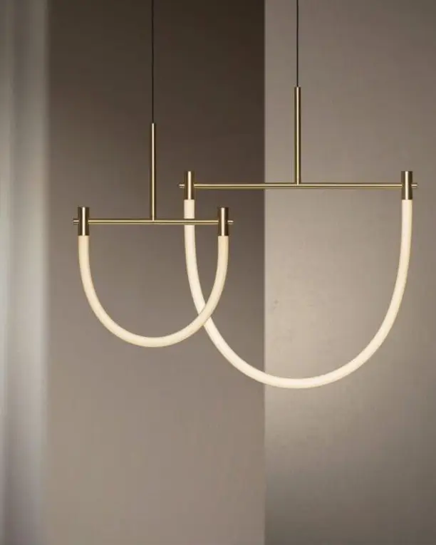 Twee gebogen lichtlijnen aan een messing frame voor een rustige grijze wand