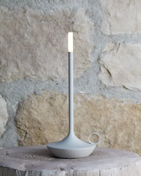Een grijze snoerloze lamp in de vorm van een kaars op een boomstronk voor een muur van natuursteen