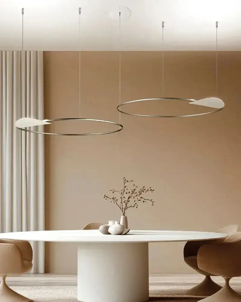 Twee lichtringen boven een ovale witte tafel in een warme beige kamer