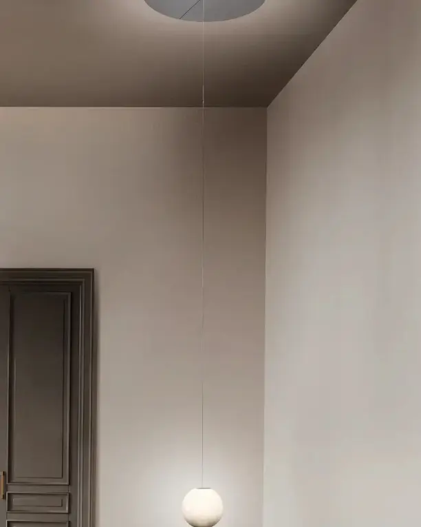 Een witte glazen bol aan een lange pendel in een hoge kamer met een donkere deur