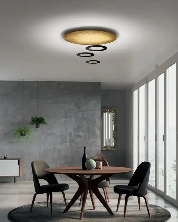 Een ronde schijf in bladgoud met ringen eronder boven een ronde eettafel met zwarte stoelen