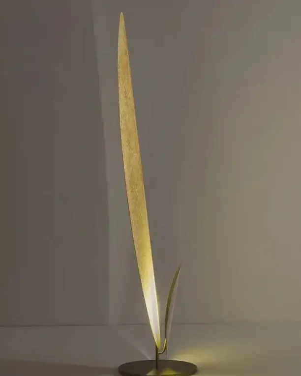 Een staande lamp als een smal gouden blad dat van onderen wordt verlicht
